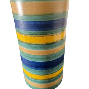 May include: A tall, cylindrical vase with horizontal stripes in shades of green, tan, blue, and yellow. The ceramic vase has a glossy finish and a slightly flared top. The design is a modern take on a classic striped pattern.
