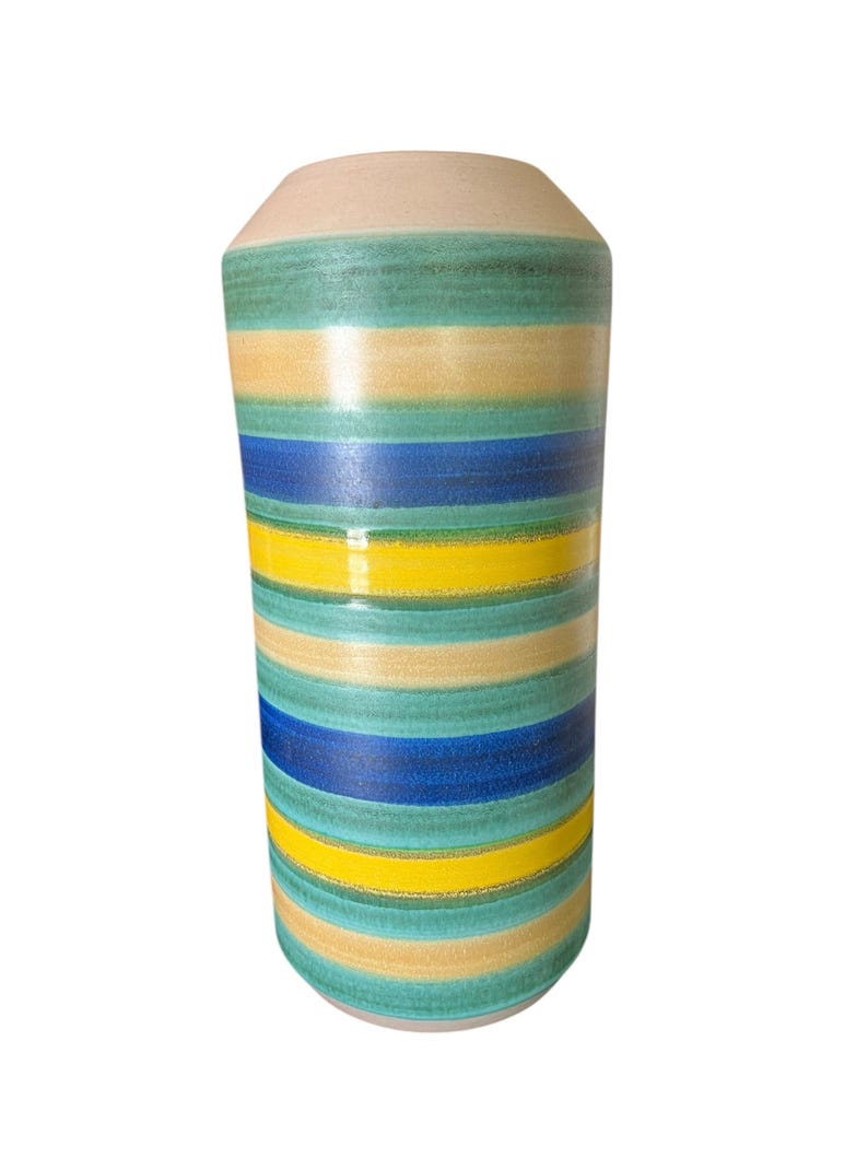May include: A cylindrical ceramic vase with horizontal stripes in shades of blue, yellow, and green. The top and bottom of the vase are a light beige color. The vase is a decorative item.
