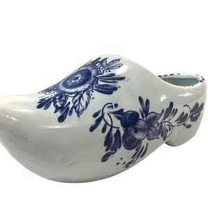 May include: A white ceramic Dutch shoe with blue and white floral designs. The shoe is a traditional Dutch souvenir.