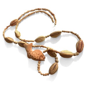 May include: A light brown necklace featuring a carved fish pendant and multiple oval-shaped beads with textured, grooved patterns. The beads are strung together in a continuous loop, showcasing a uniform tan color and intricate detailing on each piece.