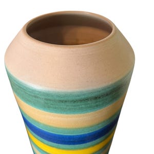 May include: A tall, ceramic vase with a wide opening and a rounded body. The vase features horizontal stripes in shades of blue, yellow, and green, with a beige top. The vase is likely used for decorative purposes.