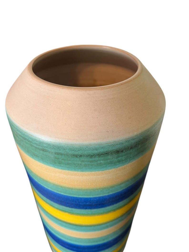 May include: A tall, ceramic vase with a wide opening and a rounded body. The vase features horizontal stripes in shades of blue, yellow, and green, with a beige top. The vase is likely used for decorative purposes.