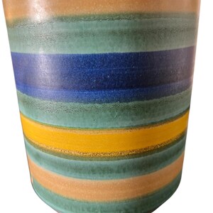 May include: A ceramic vase with horizontal stripes in shades of teal, orange, yellow, and blue. The vase has a slightly textured surface and a rounded base. The color bands are evenly spaced, creating a modern, decorative look.
