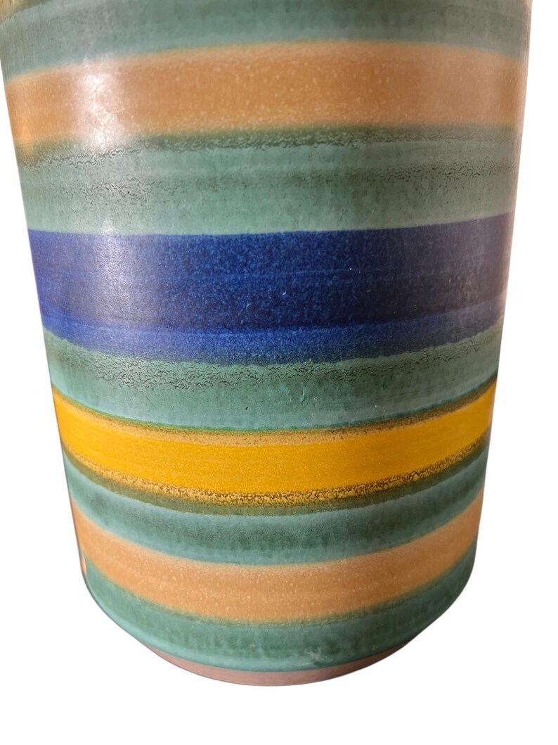 May include: A ceramic vase with horizontal stripes in shades of teal, orange, yellow, and blue. The vase has a slightly textured surface and a rounded base. The color bands are evenly spaced, creating a modern, decorative look.