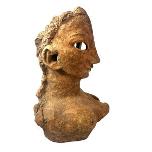 May include: A terracotta bust of a woman's head and shoulders. The bust is weathered and has a hole where the left eye would be.