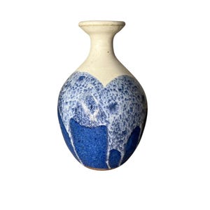 May include: A ceramic vase with a cream-colored top and a blue, textured design. The blue section has a drip-like pattern, transitioning from a lighter shade to a deep blue at the base. The vase has a narrow neck and a rounded body.