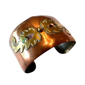 Pode incluir: Pulseira de punho de cobre com detalhes de folhas douradas. A pulseira larga apresenta um design curvo e um acabamento polido. Os detalhes de folhas douradas são colocados na frente. Um acessório de estilo vintage.