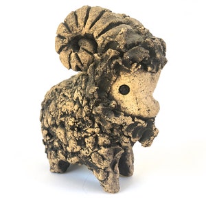 Puede incluir: Una escultura de cerámica de un carnero con un acabado texturizado marrón y dorado. El carnero tiene un cuerno grande y rizado y una cara pequeña y redonda.