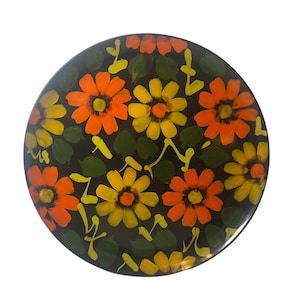 May include: A round black plate with a floral design. The flowers are orange, yellow, and green.