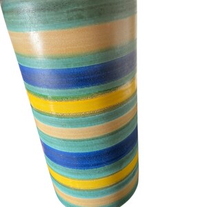 May include: A cylindrical ceramic vase with horizontal stripes in shades of blue, yellow, green, and tan. The vase has a slightly textured surface and a light beige top.