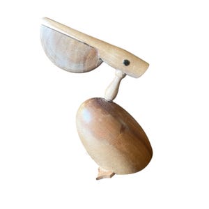 May include: A wooden pelican sculpture with a hinged beak and a small black eye. The bird is made of light brown wood and has a smooth finish. The pelican is a decorative item.