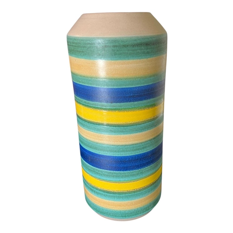 May include: A tall, cylindrical vase with a beige top and a body adorned with horizontal stripes. The stripes alternate between shades of blue, yellow, and green. The vase is approximately 10 inches tall.