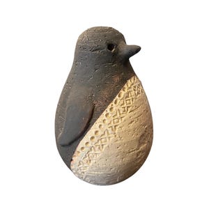 May include: A ceramic penguin ornament with a textured finish. The penguin is mainly dark grey with a cream-coloured section featuring an embossed geometric pattern. The beak is black, and the ornament has a small, rounded body.