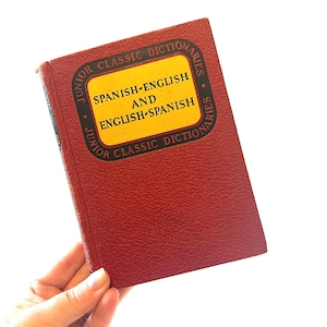 May include: A red hardcover book with a yellow label that reads "Junior Classic Dictionaries Spanish-English and English-Spanish".