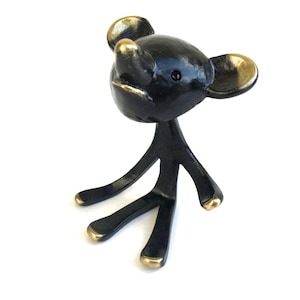 May include: A black and gold metal figurine of a stylized mouse with long legs and large ears. The mouse is sitting with its head tilted up.