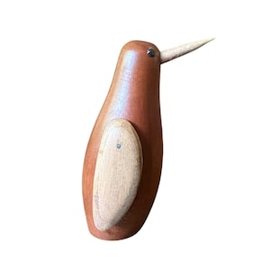 May include: A wooden bird ornament with a brown body and a pale beak. The bird has a light-coloured oval patch on its side. The figurine is a decorative item, likely for display.