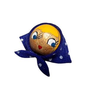 Puede incluir: Cabeza de muñeca de madera pintada a mano con un pañuelo azul con lunares blancos. La muñeca tiene pelo amarillo, ojos azules y boca roja. La cabeza está pintada con tonos dorados y marrones.