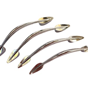 Puede incluir: Cuatro tiradores de puerta de armario plateados con un diseño en forma de hoja. Los tiradores son curvos y tienen un acabado pulido.