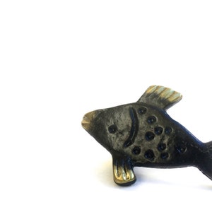 Può includere: Una maniglia o tirare per porta a forma di pesce nero e dorato. Il pesce ha un design stilizzato con un corpo nero e accenti dorati.