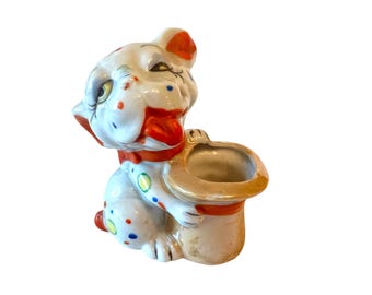 Peut inclure: Une figurine en céramique blanche d'un chien portant un chapeau rouge et blanc. Le chien a des pois noirs et bleus et une langue rouge qui sort. Le chapeau a un intérieur blanc et est en forme de chapeau haut de forme.