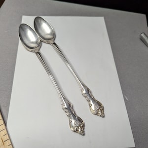 May include: Two silver spoons with ornate handles. The spoons have a rounded bowl and a long, slender handle.