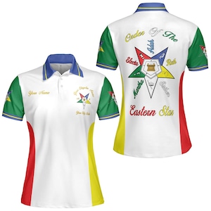 Puede incluir: Polo blanco con detalles en azul, verde, rojo y amarillo. Presenta un emblema de estrella y texto en la parte delantera y trasera, incluyendo "Order Of The Eastern Star". La camisa tiene cuello y mangas cortas.