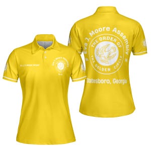 Puede incluir: Un polo amarillo con ribetes blancos en las mangas y el cuello. La parte delantera de la camisa presenta un emblema circular con texto y un gráfico de paloma. La parte trasera muestra un emblema más grande y el texto "Eva J. Moore Assembly, The Order of the Golden Circle, Statesboro, Georgia."