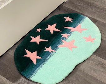 May include: A green and blue oval rug with pink stars. The rug has a gradient design with a darker green color at the top and a lighter blue color at the bottom.