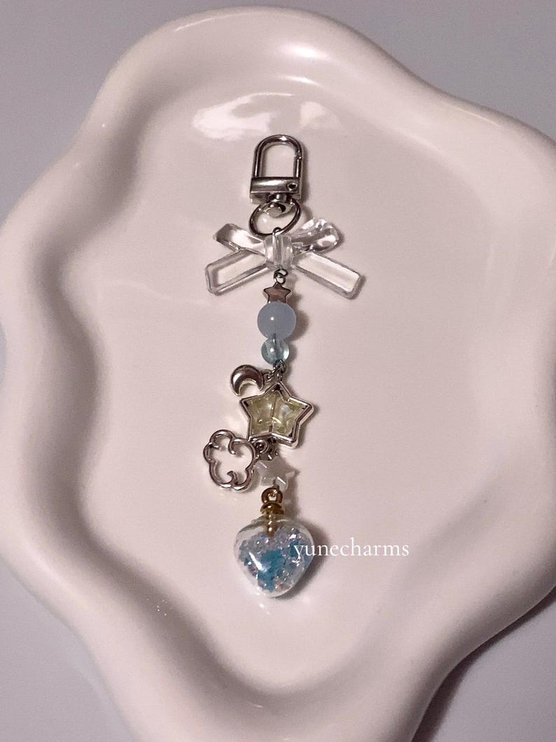 Puede incluir: Un llavero con un dije de plata, un lazo transparente, cuentas azules, una estrella plateada, una nube plateada y un dije en forma de coraz&oacute;n lleno de brillantina azul.