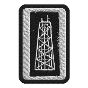 May include: Embroidered patch featuring a white outline of a tall structure, possibly a radio tower or skyscraper, against a black background. The patch has a rectangular shape with rounded corners and a white border. The design is detailed and textured.