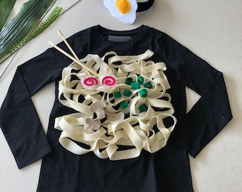 May include: A black long-sleeved shirt with a felt ramen noodle design. The noodles are white, with green onions and pink fish cakes.