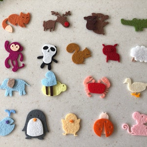 May include: A set of felt animal and insect cutouts, including a reindeer, a fox, a monkey, a panda, a squirrel, a pig, a sheep, an elephant, a bee, a crab, a duck, a whale, a penguin, a chick, a ladybug, and a mouse. The cutouts are all different colors and are arranged in a grid pattern.