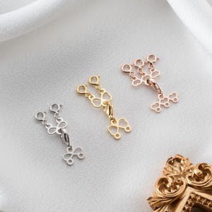 May include: Three multi-strand necklace detanglers in silver, gold, and rose gold tones. Each piece features two lobster claw clasps at the top connected to a central heart-shaped link, with a single lobster claw clasp at the bottom for attachment.