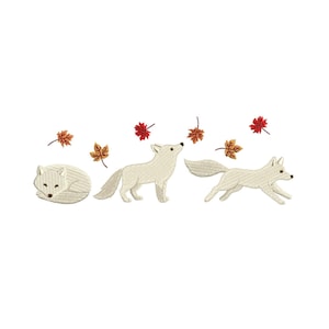 May include: An embroidered design featuring three white foxes in different poses: curled up, standing, and running. Autumn leaves in shades of red and orange are scattered around the foxes, creating a seasonal theme. The design is on a white background.