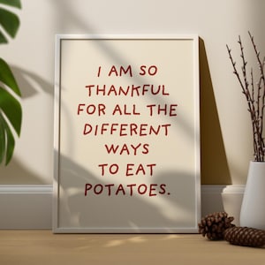 May include: White framed print with a beige background and red text that reads "I am so thankful for all the different ways to eat potatoes."