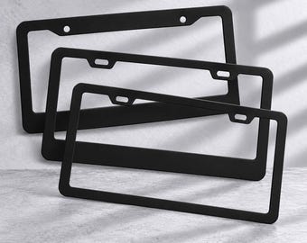 May include: A set of three rectangular matte black number plate frames. Each frame features a slim border design with two mounting holes at the top for secure attachment to a vehicle. The frames are stacked in a staggered, overlapping arrangement.