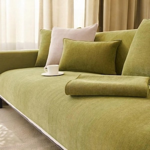 Puede incluir: Un sofá verde con un patrón de espiga, con dos almohadas y una manta. El sofá está decorado con una taza y un platillo blancos.