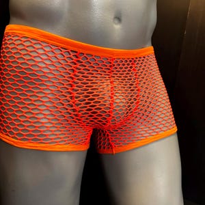 Puede incluir: Calzoncillos tipo bóxer de red en color naranja neón brillante, con una cintura elástica ancha en color naranja sólido y aberturas para las piernas a juego. La prenda está confeccionada en tejido de malla flexible con patrón hexagonal.