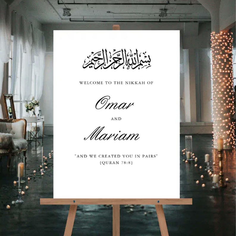 May include: A white wedding sign on a wooden easel, with black calligraphy. The sign includes Arabic script, the names "Omar" and "Mariam", and a quote from the Quran. The sign welcomes guests to the Nikah.