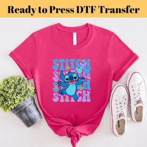 May include: A pink t-shirt with a blue Stitch character holding balloons. The text "Stitch" is repeated in a retro font.