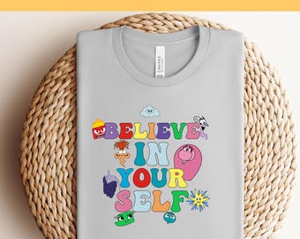 May include: A light gray t-shirt with the words "BELIEVE IN YOUR SELF" in colorful, cartoon-style lettering. The shirt also features various whimsical illustrations. The text "Ready to Press DTF Transfer" is at the top.