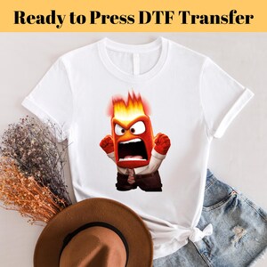 May include: White t-shirt featuring a cartoon image of a red and orange character with flames on his head. The character is shouting and has a surprised expression on his face. The text "Ready to Press DTF Transfer" is at the top of the image.