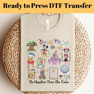 Pode incluir: Camiseta bege com um gráfico colorido da Disney Trip. O design inclui Mickey e Minnie Mouse, um castelo e outros ícones da Disney. O texto "The Happiest Place One Earth" também está impresso na camiseta. As palavras "Ready to Press DTF Transfer" estão no topo.