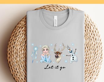 Puede incluir: Camiseta gris claro con un gráfico colorido de personajes animados, incluyendo una princesa, un reno y un muñeco de nieve. Las palabras "Let it go" están escritas en una fuente de escritura debajo de los personajes. El texto "Ready to Press DTF Transfer" está en la parte superior.