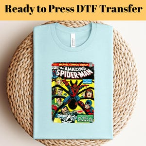 May include: A light blue t-shirt with a vintage comic book print of The Amazing Spider-Man. The comic book cover features Spider-Man in red and blue, with black webbing, and the Punisher in black and white. The text on the cover reads "The Amazing Spider-Man" and "Return of the Punisher!"