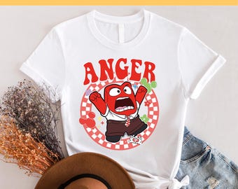 May include: White t-shirt with a red cartoon character with the word "ANGER" printed above it. The character is wearing a white shirt and brown pants. The character is surrounded by a red and white checkered circle with flowers and a Mickey Mouse head.