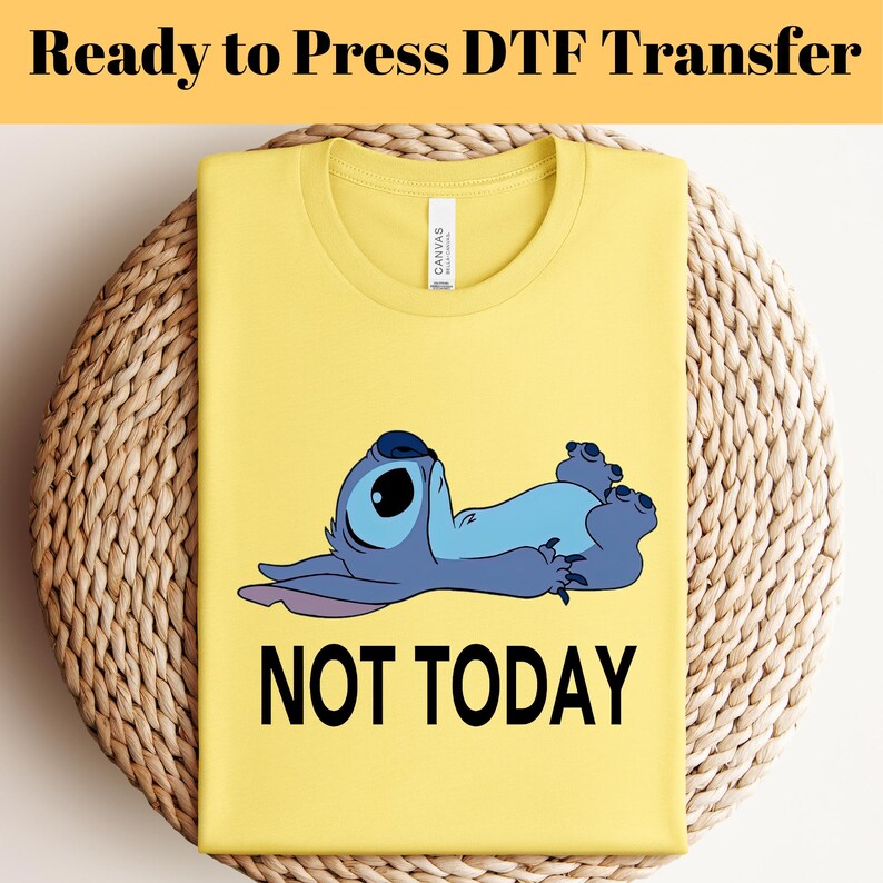 K&ouml;nnte beinhalten: Gelbes T-Shirt mit einer Cartoonfigur in Blau und Schwarz und den Worten "NOT TODAY" in Schwarz. Das T-Shirt liegt auf einer gewebten Oberfl&auml;che. Der Text "Ready to Press DTF Transfer" steht oben.