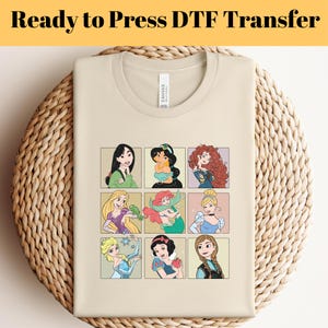 May include: A beige t-shirt featuring nine cartoon illustrations of princesses in a grid pattern. The text "Ready to Press DTF Transfer" is at the top of the image. The shirt is folded on a woven surface.