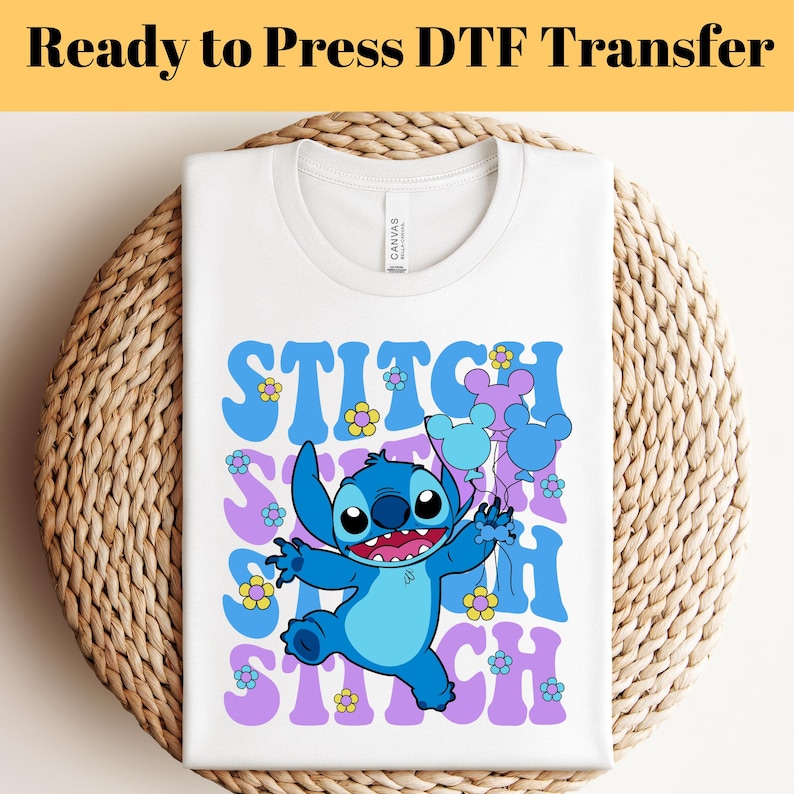 May include: White t-shirt with a blue Stitch character holding balloons with Mickey Mouse ears. The text "Stitch" is repeated in a purple and blue retro font with yellow flowers.