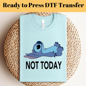 K&ouml;nnte beinhalten: Hellblaues T-Shirt mit einem Cartoon-Charakter und dem Text "NOT TODAY" in Schwarz. Das T-Shirt liegt auf einer gewebten Unterlage. Der Text "Ready to Press DTF Transfer" befindet sich oben im Bild.